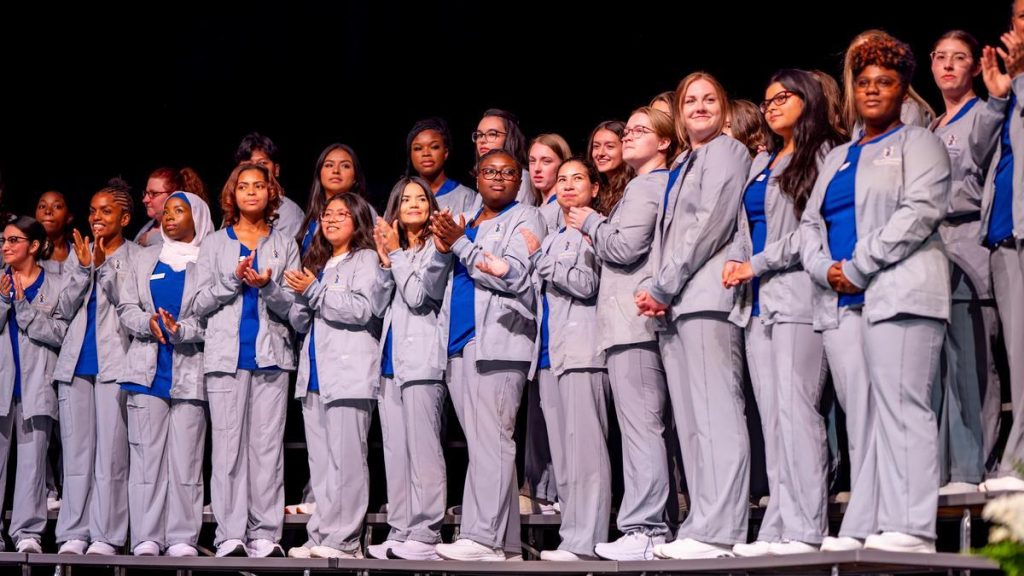 Nursing students in white coats in a row on stage