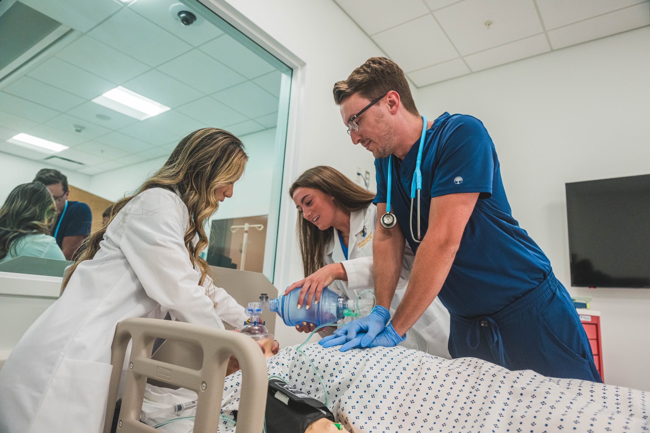 Three nursing students conduct a practice drill in a clinical lab setting